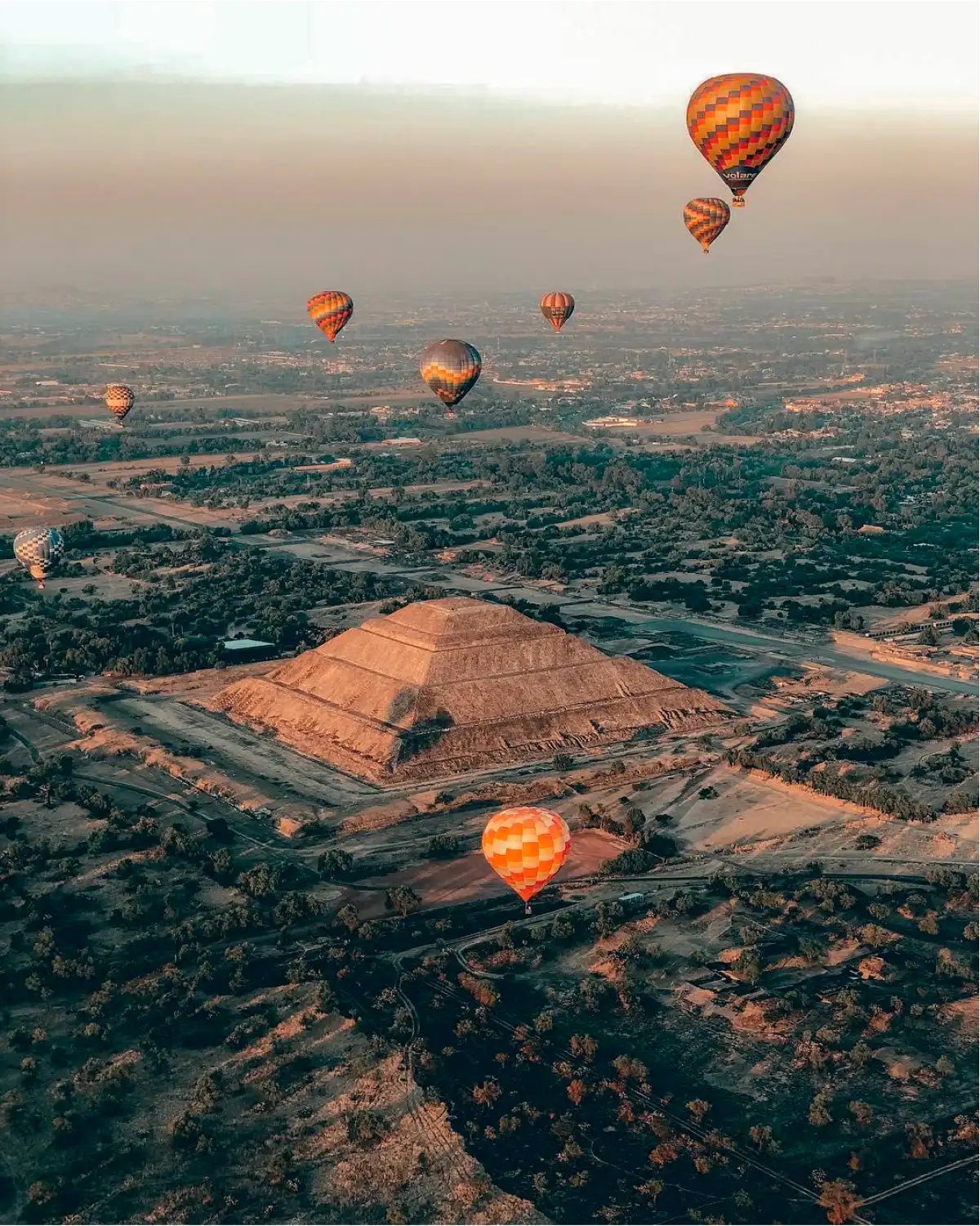 Aerial view at dawn of the Pyramid of the Sun at Teotihuacán, with hot air balloons floating over the valley in golden light
