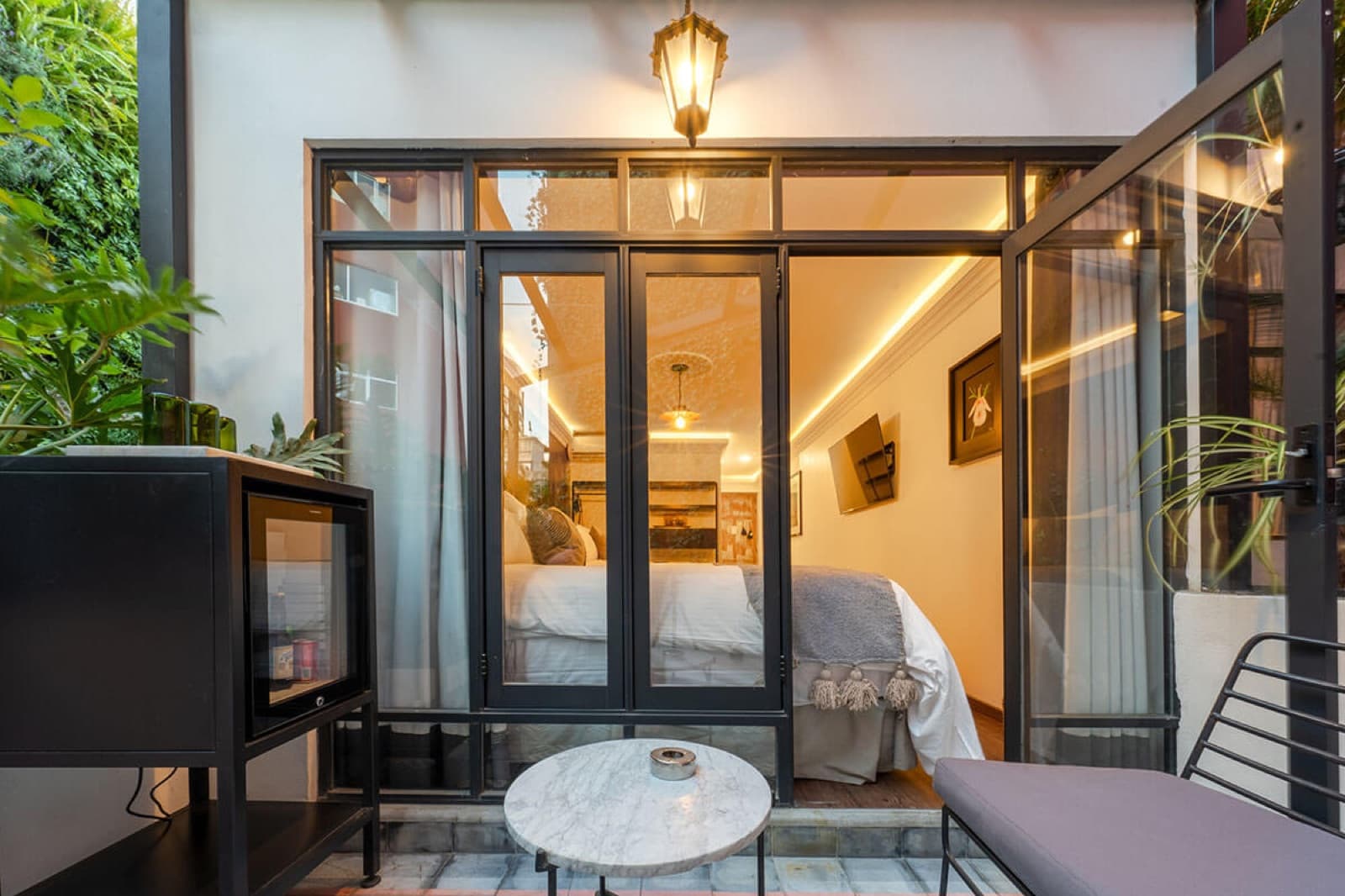 Private terrace of the house at dusk, with the lit steel doors and a brass lantern