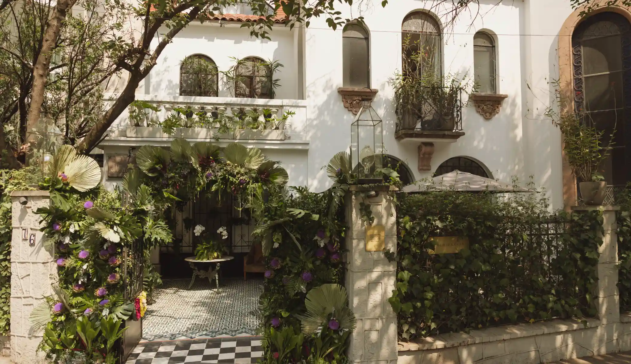 The entrance to Orchid House Polanco from the street, with the arch of flowers and palm leaves over the gate and the chequered floor of the entrance