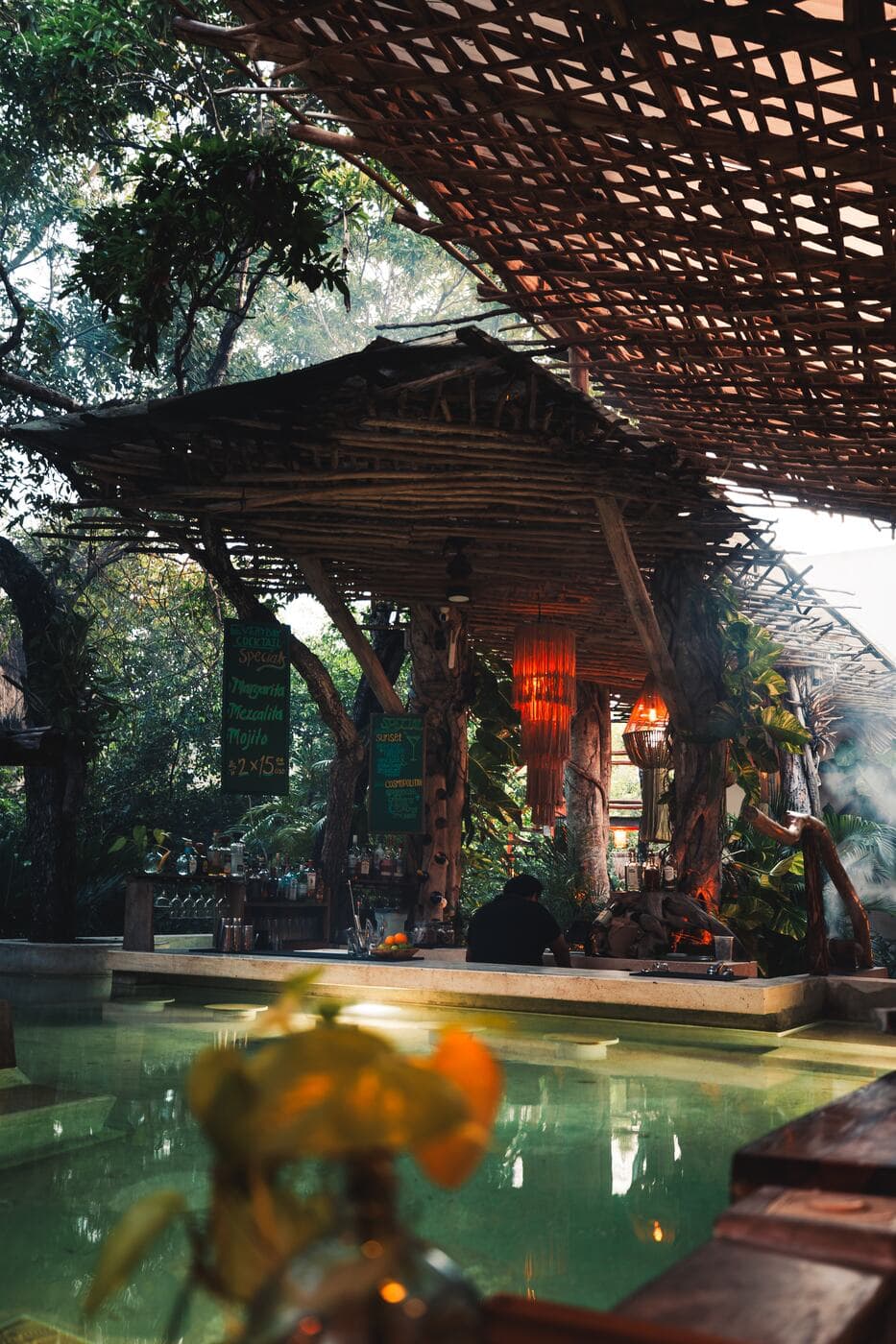The bamboo structure above the pool at dusk, its lamps lit among the tree trunks