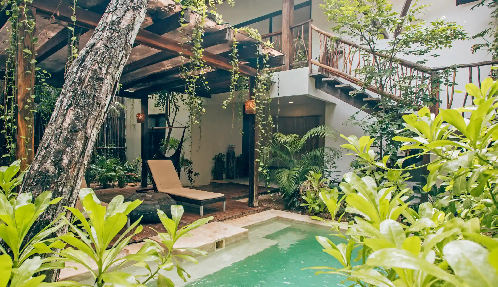 The pool amid the jungle, with a vine-railed staircase, a sun lounger and a hammock under the pergola