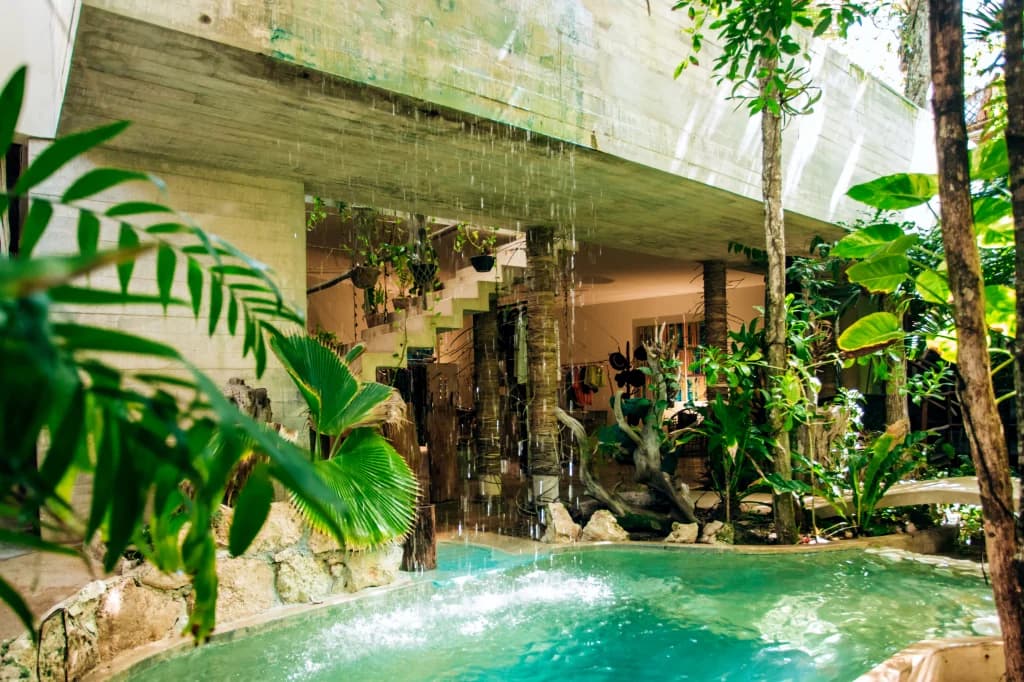 A concrete cascade falls into the pool amid the jungle, with the lobby staircase beyond