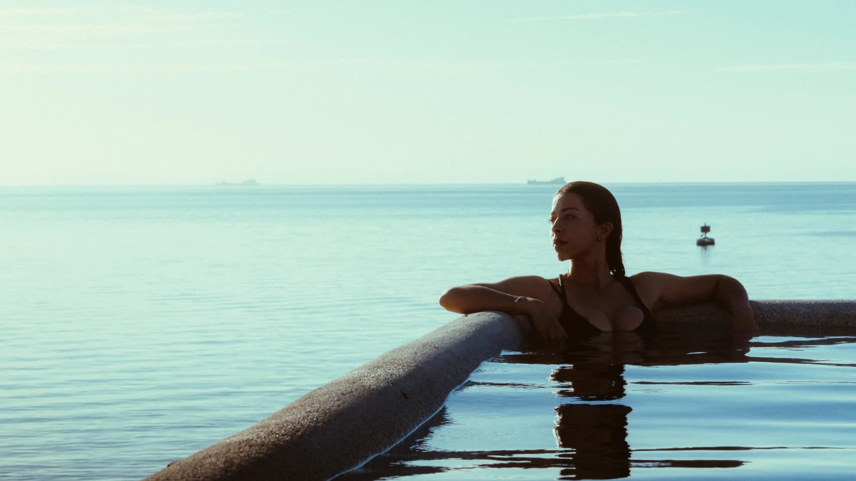 A guest rests at the edge of the infinity pool, arms resting on the ledge, the calm sea stretching out beyond