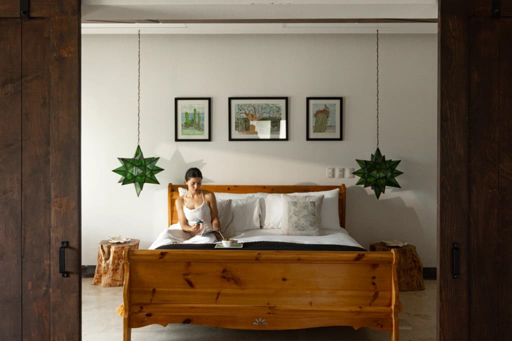 A guest has breakfast sitting on a solid wood bed, between two star-shaped pendant lamps and cactus artwork on the wall, framed by the wooden sliding doors