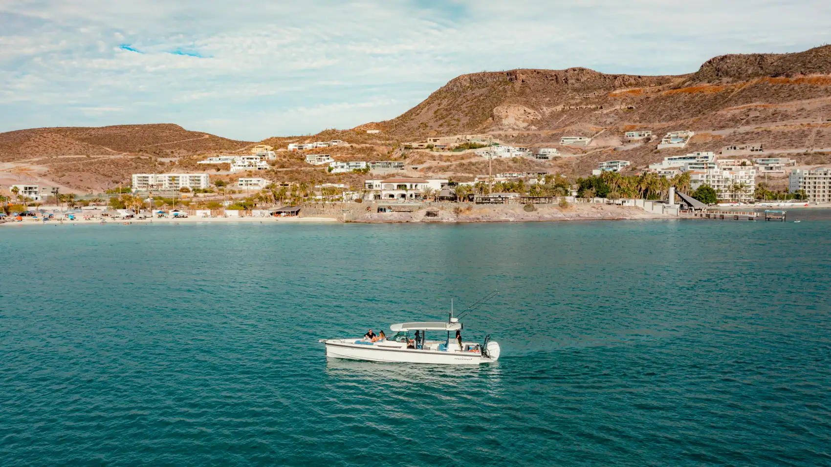 A boat with passengers cruising La Paz's turquoise bay, the built-up coastline and desert hills behind