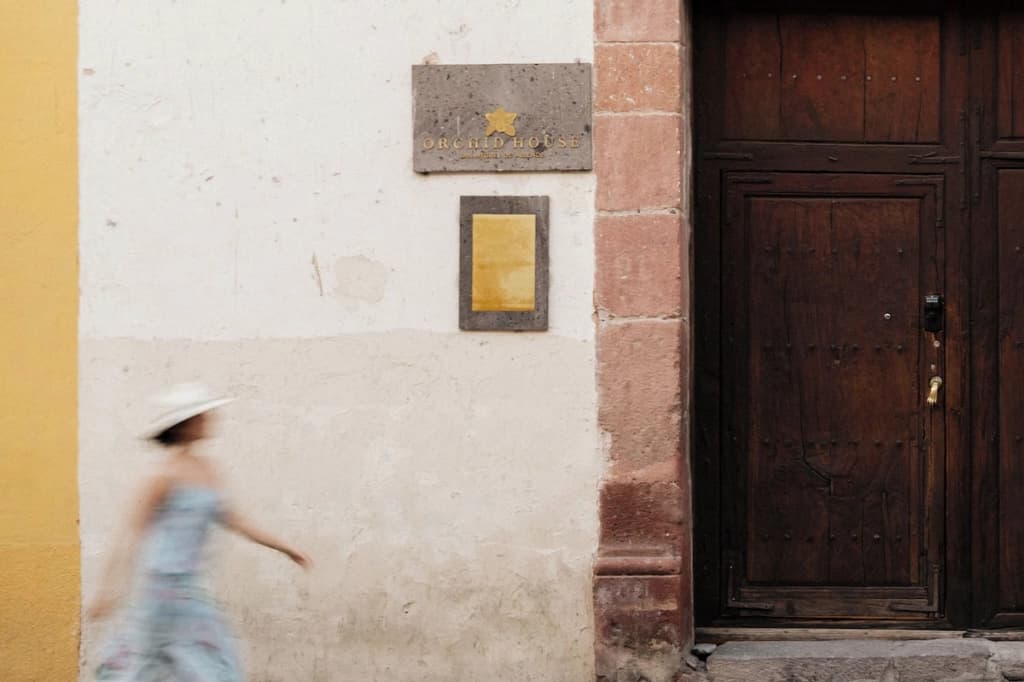 The house's entrance from the cobblestone street: the gold «Orchid House» plaque beside the wooden door, a guest passing by