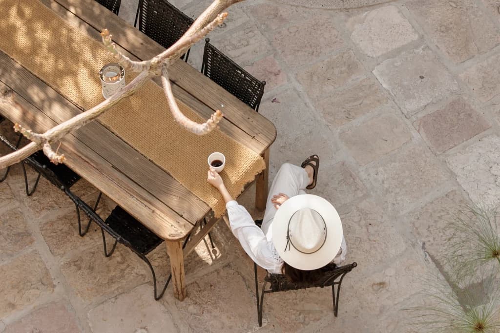 An overhead view of a guest in a hat having coffee at the courtyard table, on the cobblestone floor