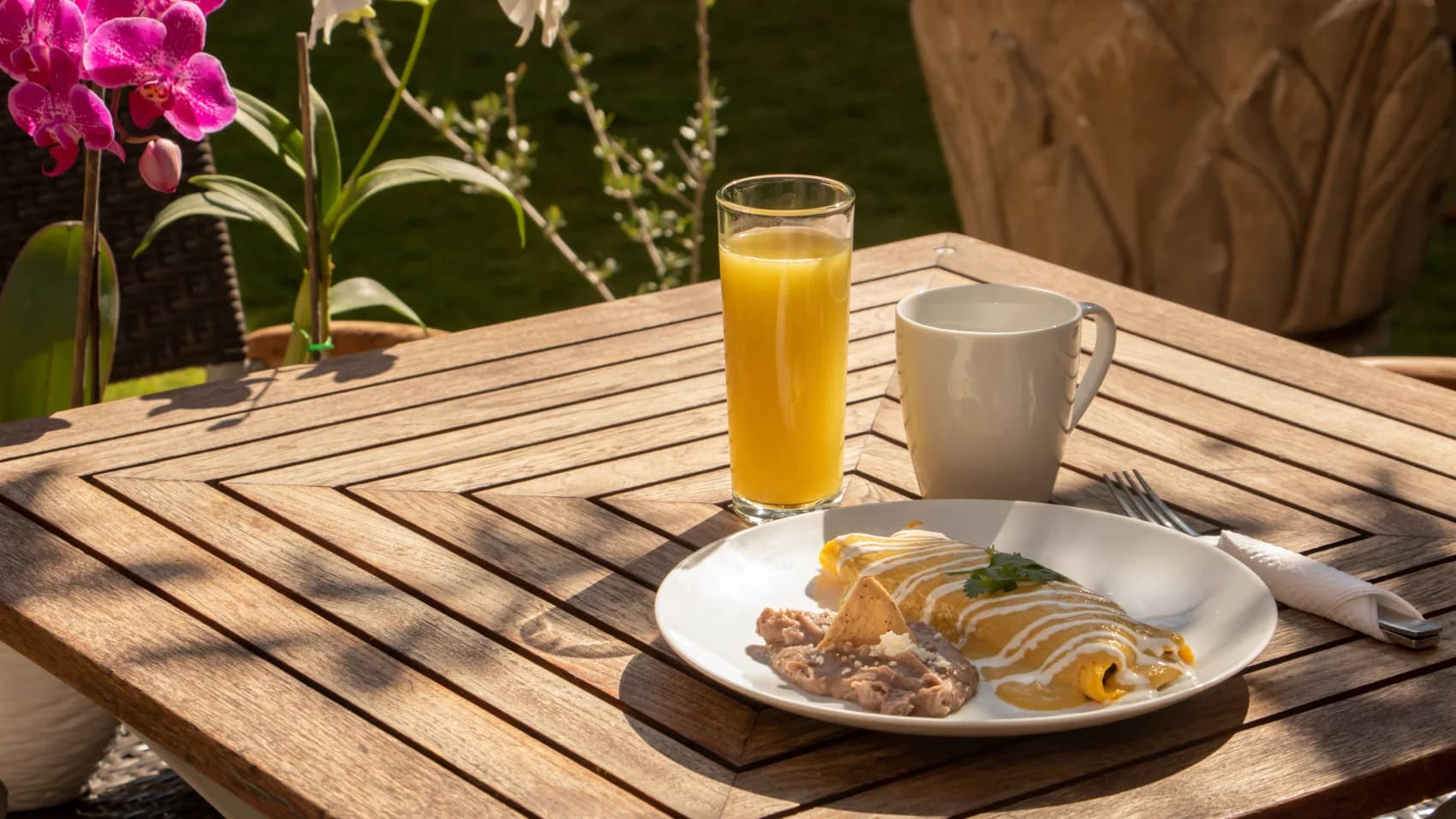 Green enchiladas with refried beans, orange juice and coffee on the garden table, beside a magenta orchid