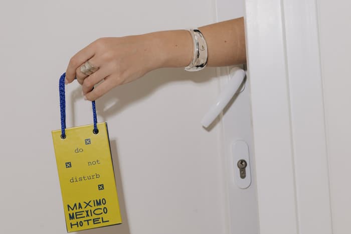 A hand hanging Máximo México Hotel's yellow do-not-disturb tag on the door handle