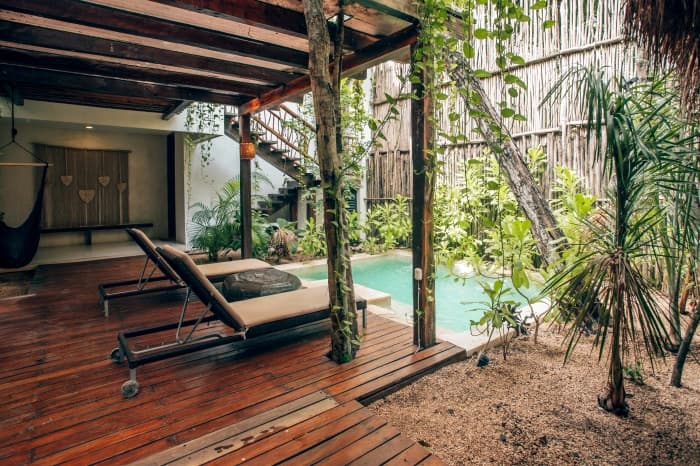 Wooden loungers beside the private pool, under the timber pergola and thatch wall, surrounded by jungle