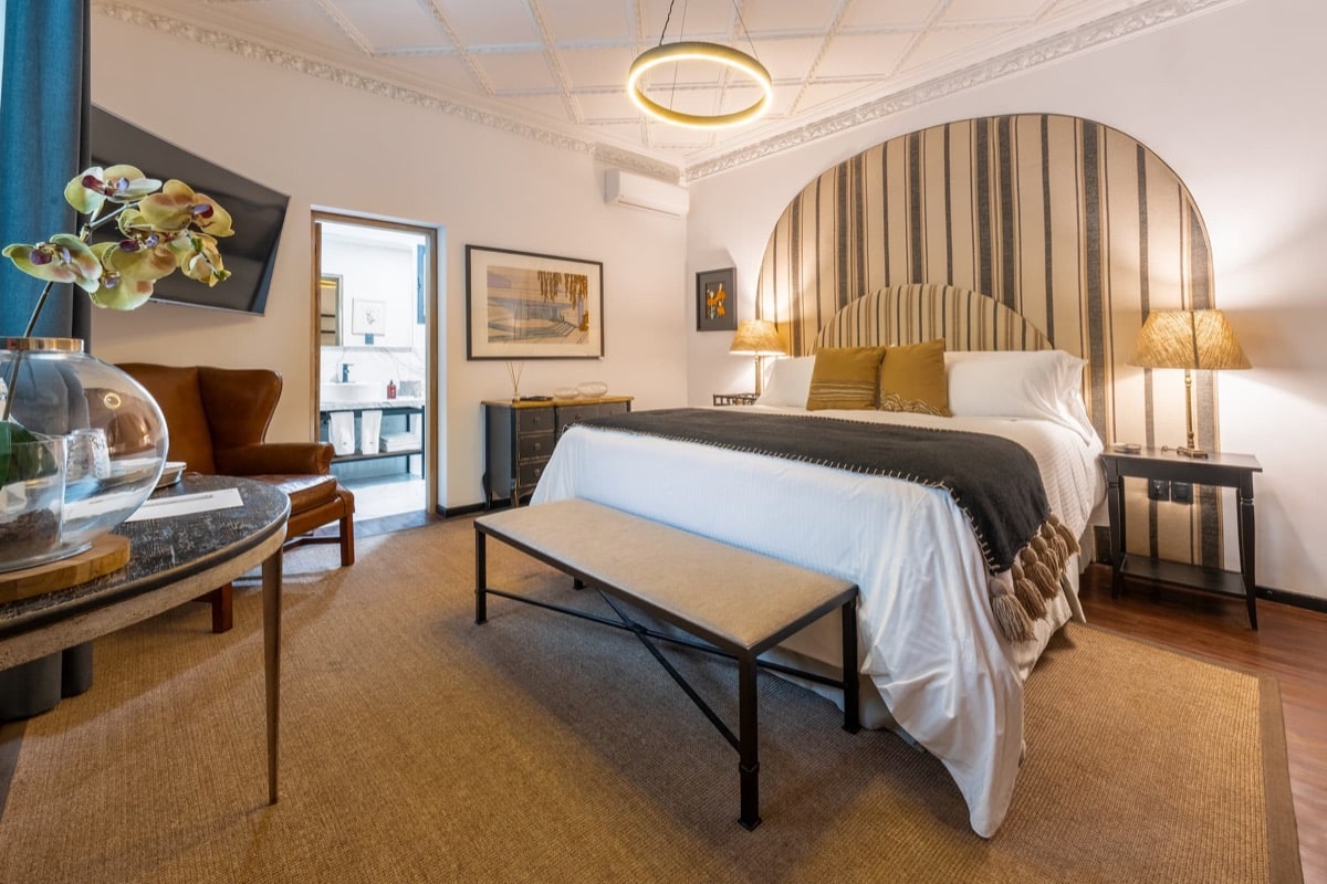 Room with a striped arched headboard, a reading chair and an en-suite bathroom