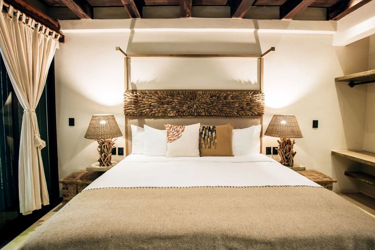 A suite with a king bed under a brass canopy frame and a driftwood headboard, between two wicker lamps