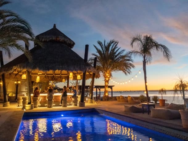 El Caimancito's palapa bar at dusk, with guests seated and the pool facing the sea