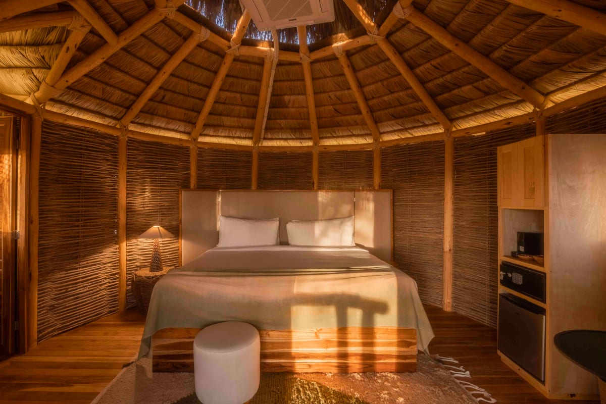 Inside the round bungalow: reed walls, a conical roof of timber and palm, a king bed and a minibar
