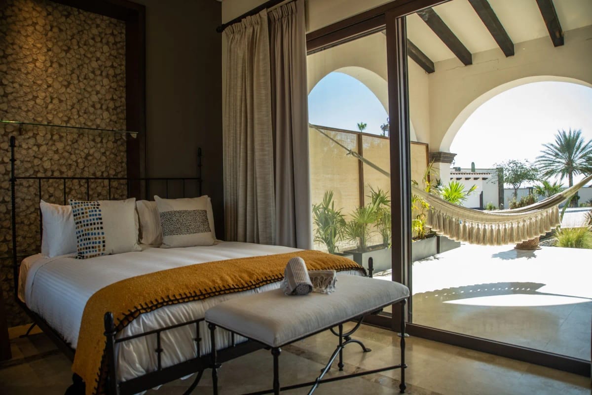 Room with a wrought-iron bed and mustard throw, a river-stone wall and sliding doors onto a patio with a hammock