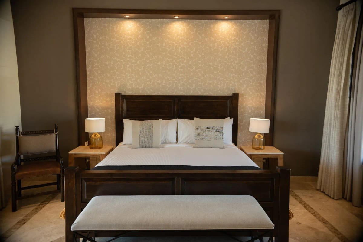 Room with a dark timber king bed, a lit upholstered headboard panel and a bench at the foot