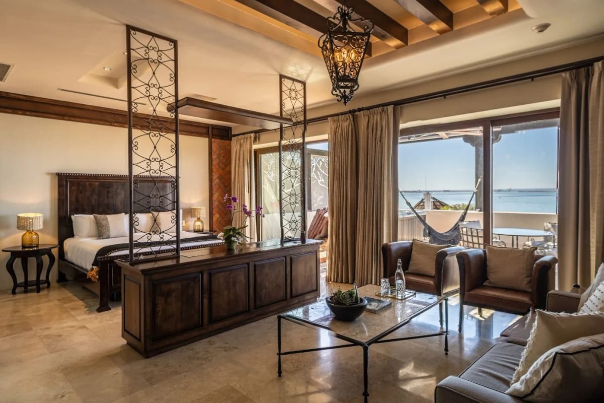 Master suite with a wrought-iron four-poster bed, a sitting area with leather armchairs and a terrace with a hammock over the sea