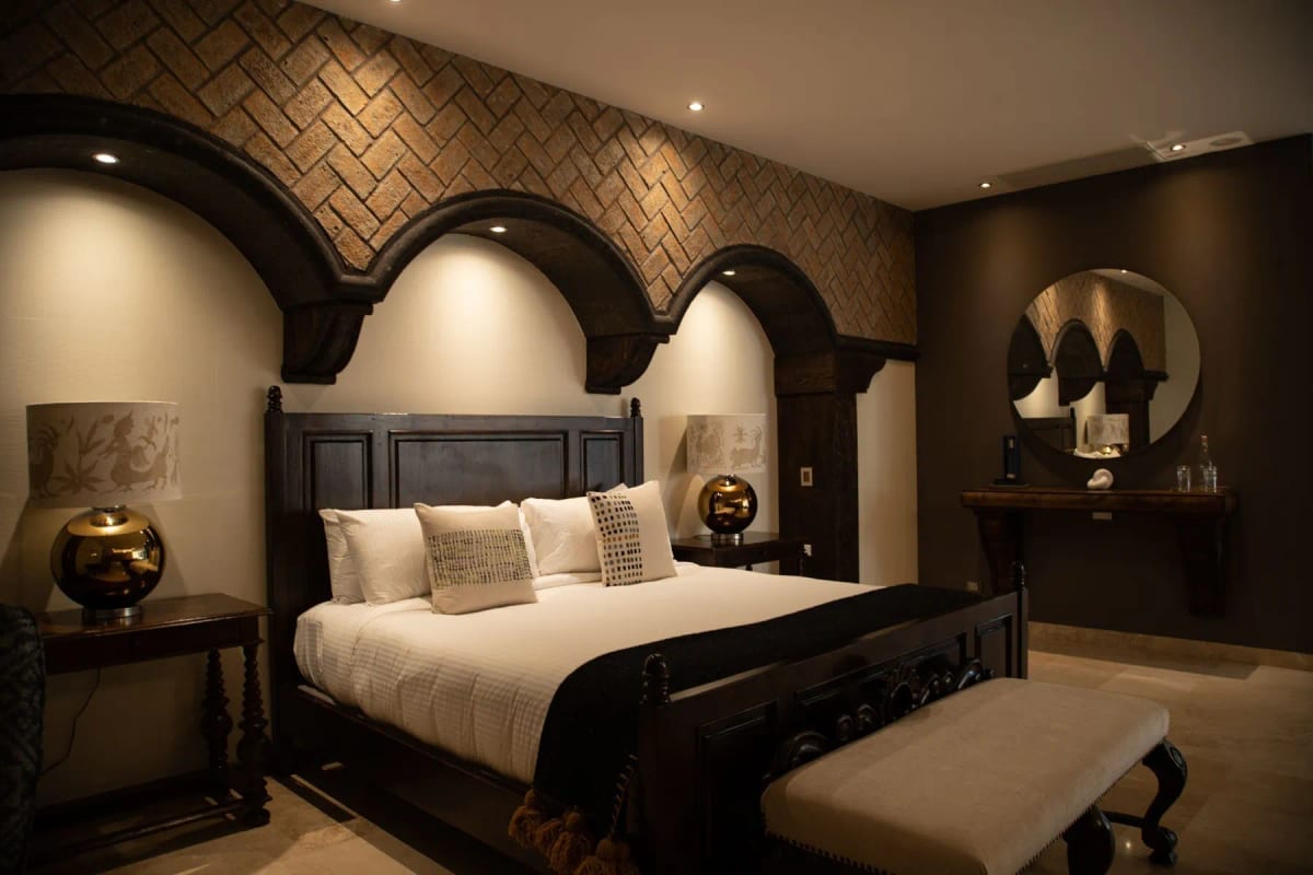 Presidential suite with an arched timber headboard under a brick wall, a console table and a round mirror