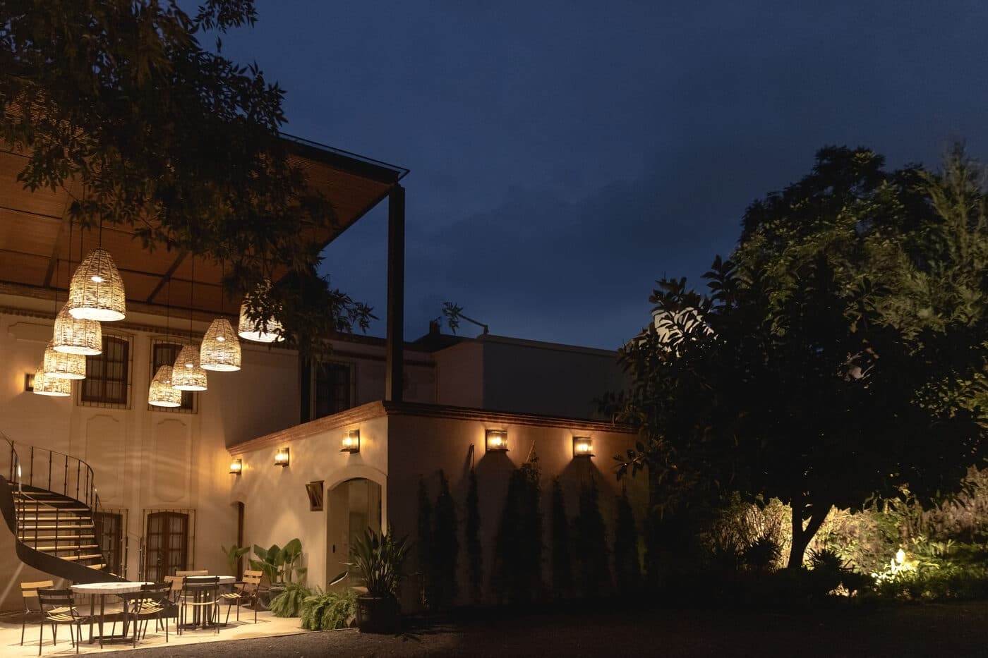 El patio al anochecer, con el cielo todavía azul, las luces encendidas sobre el muro y los cipreses en sombra