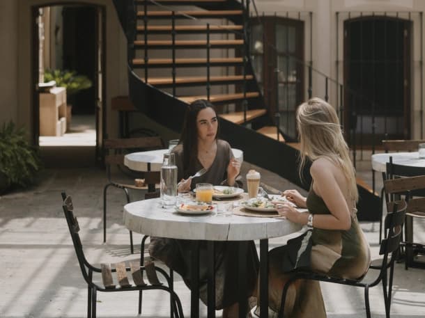 Two guests have breakfast at a courtyard table, beside the spiral staircase