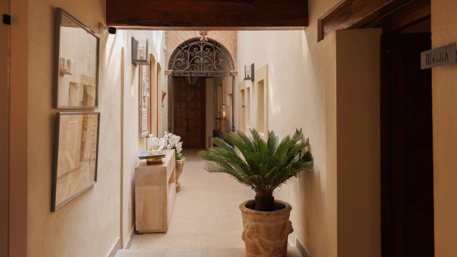 Corredor interior con obra enmarcada, una consola con orquídeas y una palma, junto a la puerta de una de las habitaciones