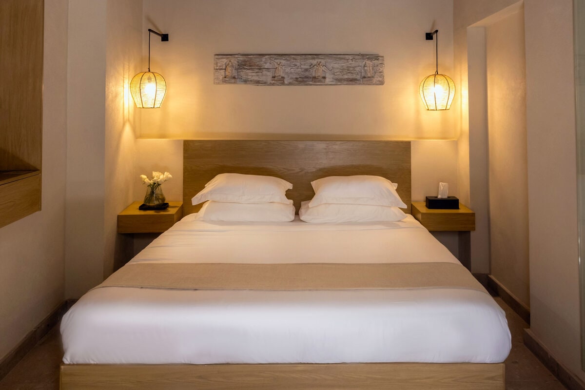 Recámara con cama king bajo un tablón horizontal desgastado, entre dos lámparas de mimbre