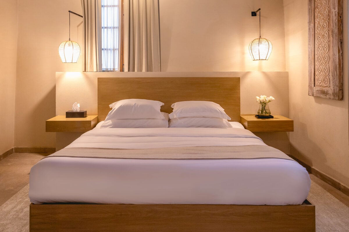 Recámara con cama king entre dos lámparas de mimbre, con una ventana con cortina detrás de la cabecera