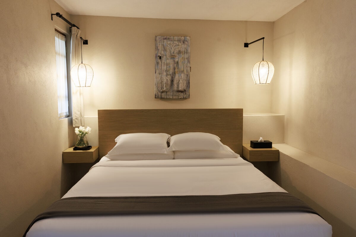 Recámara con cama king bajo una tabla de madera desgastada, entre dos lámparas de mimbre