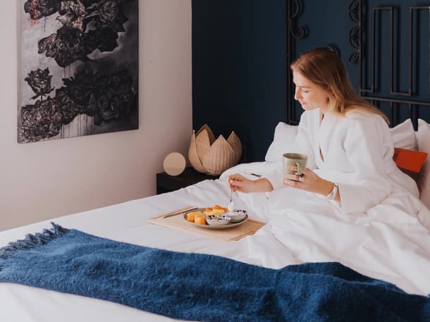 Breakfast in bed: a tray of fruit, the guest in a robe with a cup of coffee, against the dark headboard and lotus lamps