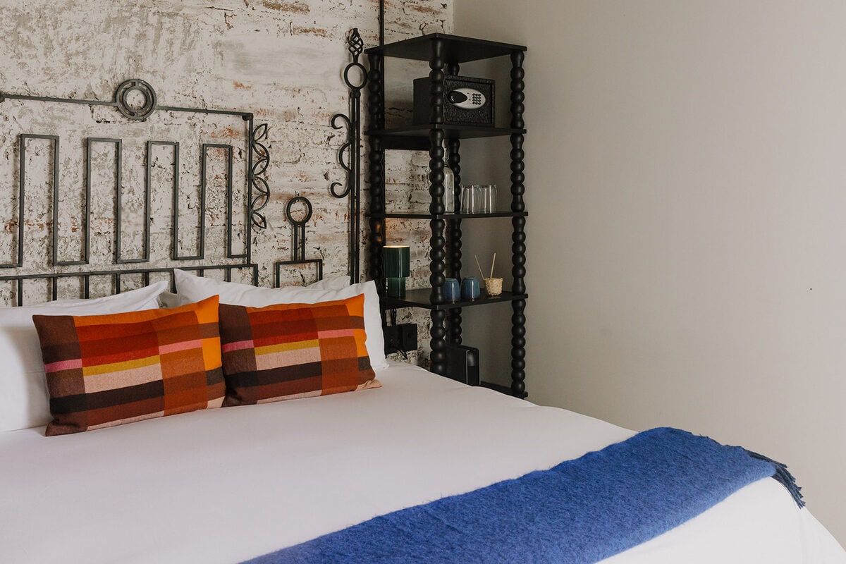 A King bed against a whitewashed brick wall, with a turned black shelf