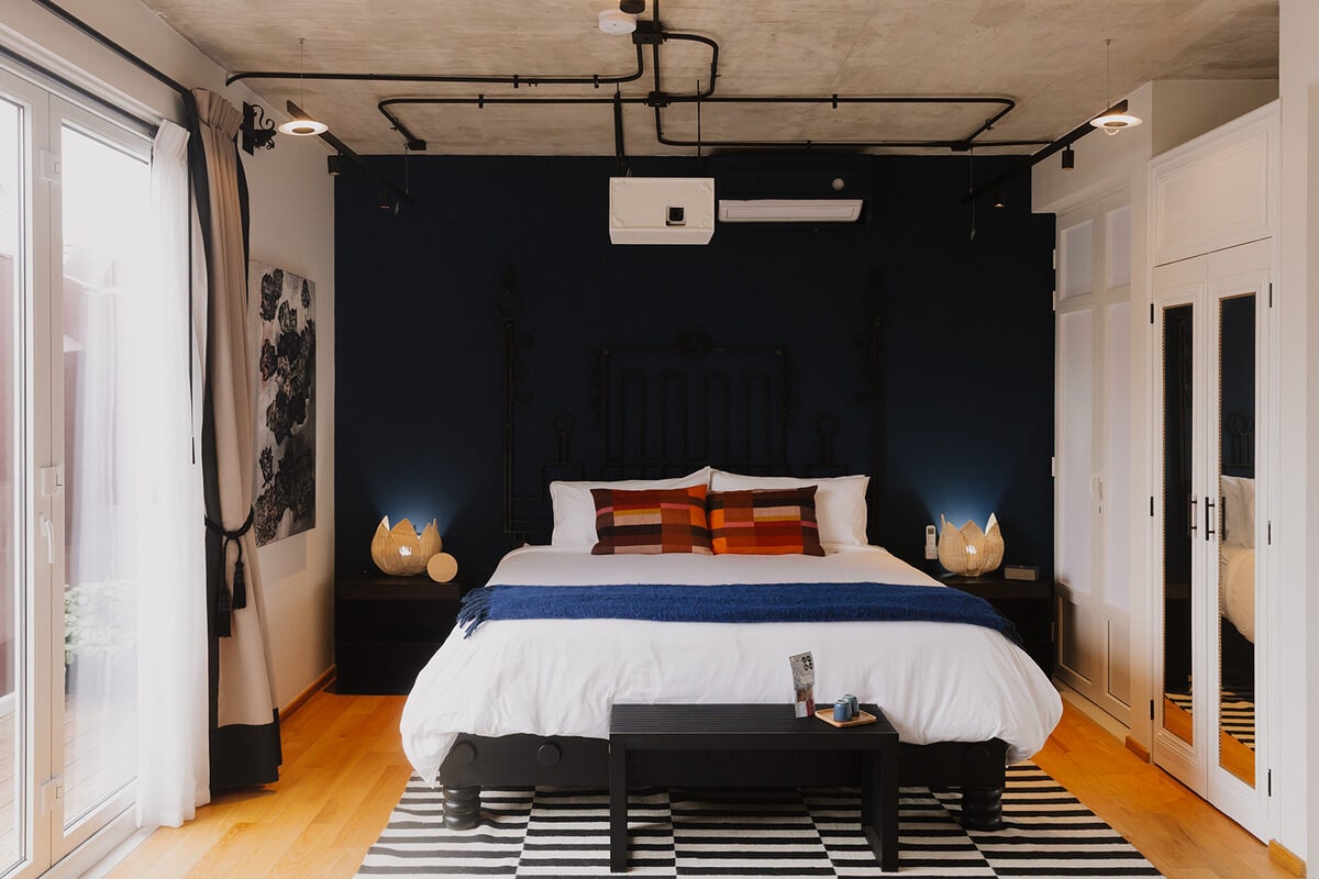 A King bed under an exposed concrete ceiling, with the projector visible above