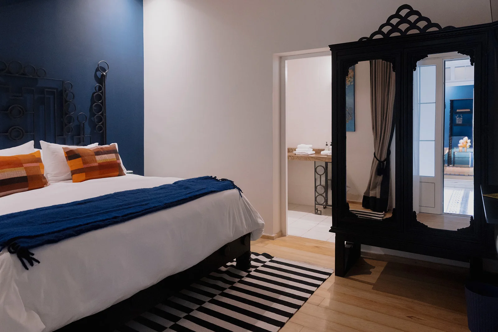 Room with a blue wall and a striped rug, and the open door to the separate bathroom with its marble basin