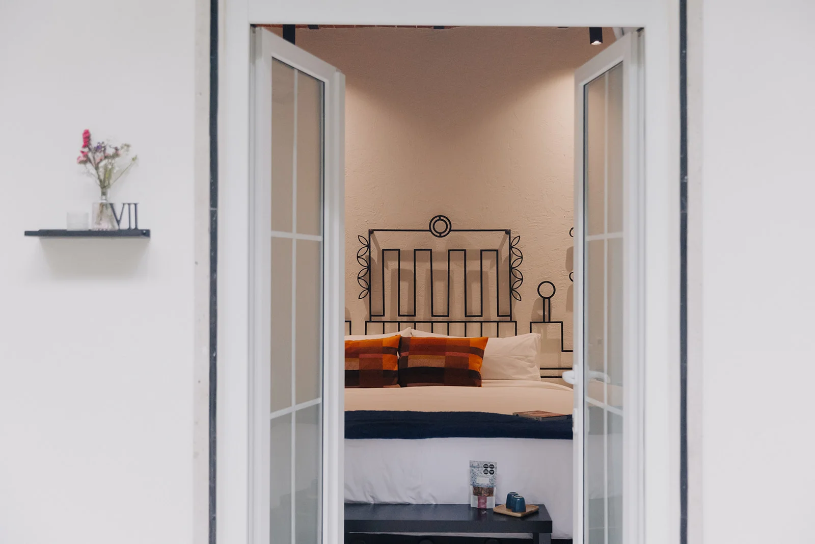 The bedroom seen through the open French doors, with the King bed and its wrought-iron headboard beyond