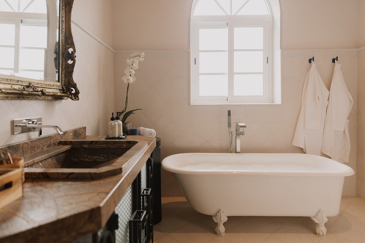 A freestanding tub under an arched window, beside a veined marble basin