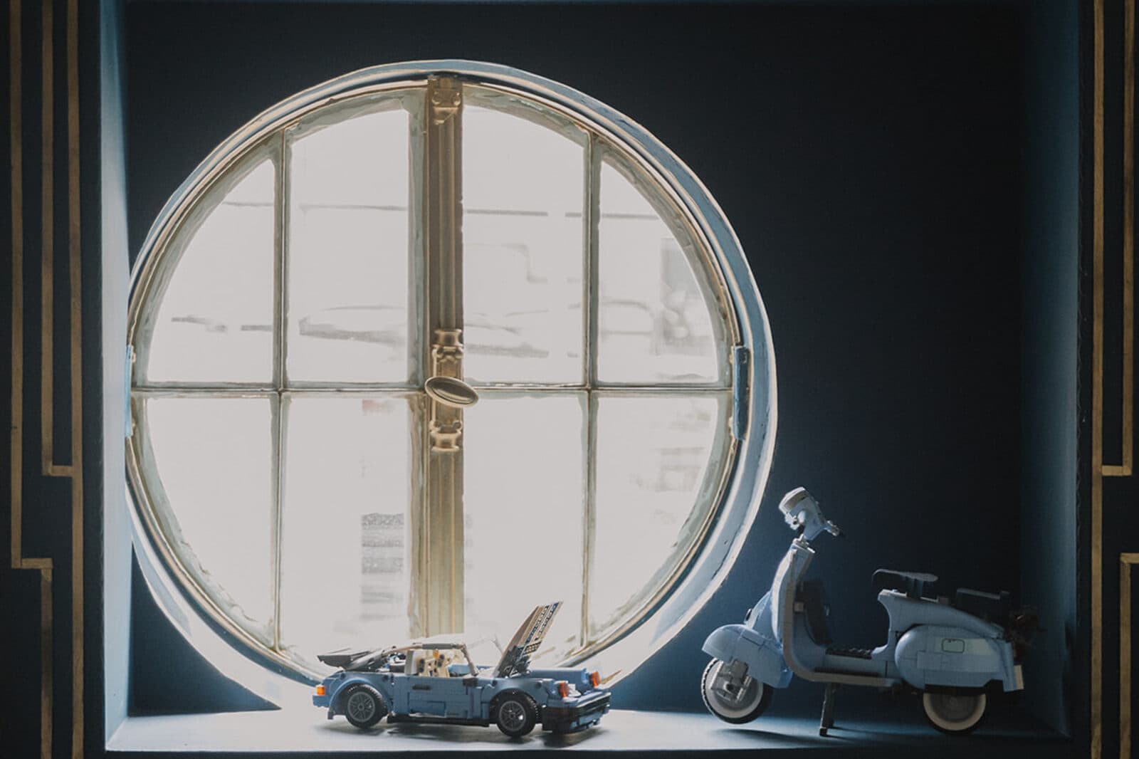 The house's entrance hall: a circular porthole window, and on the sill a blue Vespa and a blue Volkswagen in miniature