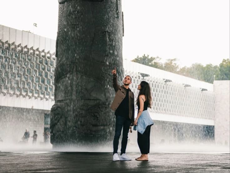 A couple in front of the "El Paraguas" monolith at the National Museum of Anthropology, amid the curtain of water