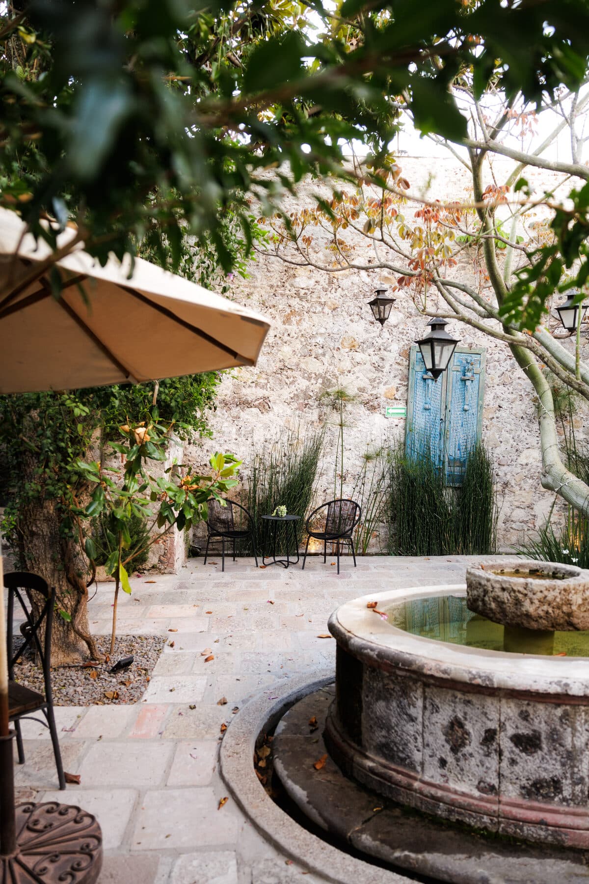The courtyard with its cantera stone fountain, a canvas parasol and the blue door on the stone wall
