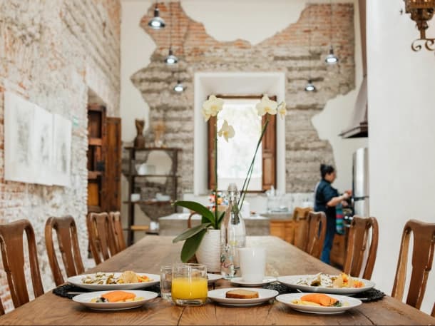 The long wooden table laid for breakfast, with an orchid centrepiece and the exposed brick wall behind