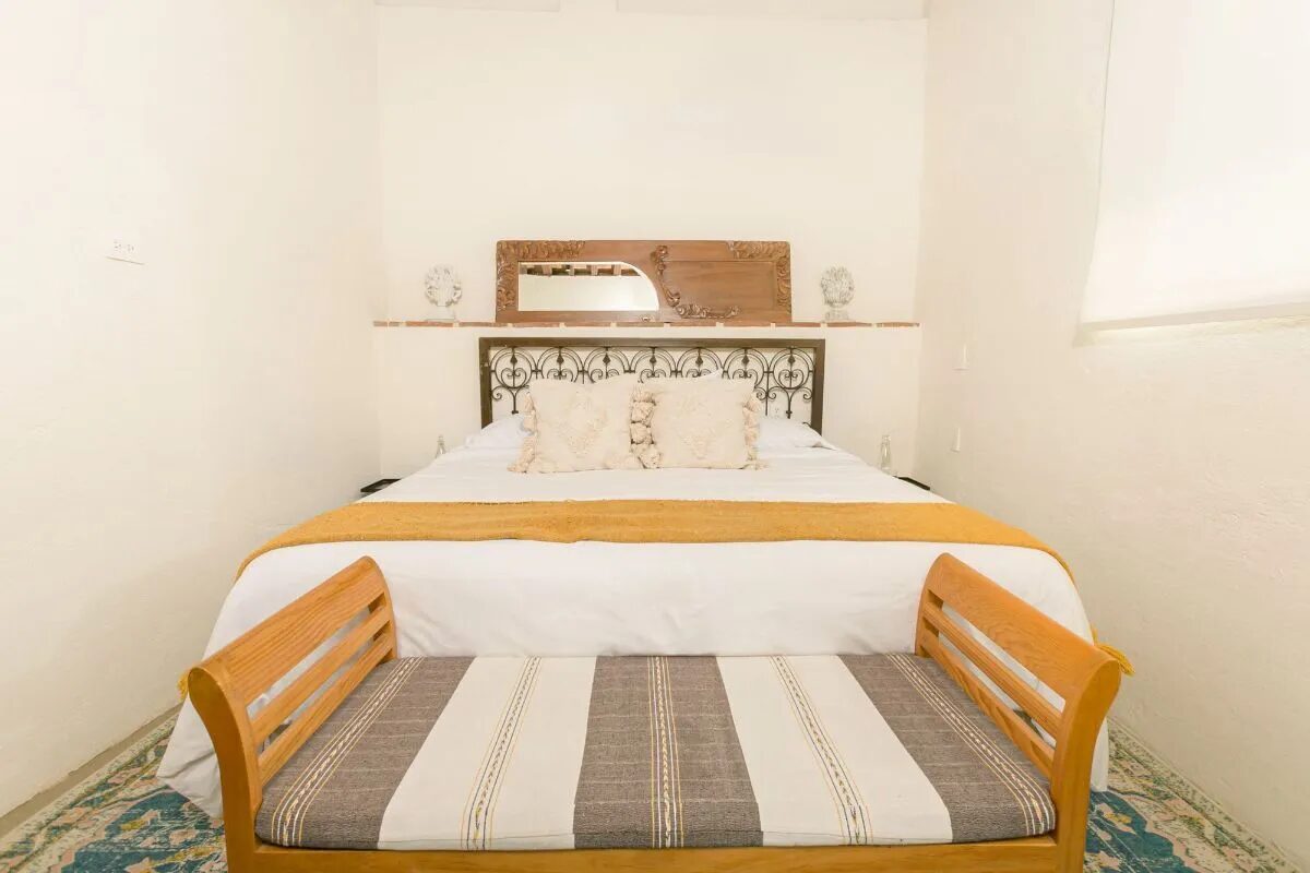 Room with a wrought-iron headboard, an antique carved mirror on the ledge above and a timber bench at the foot of the bed