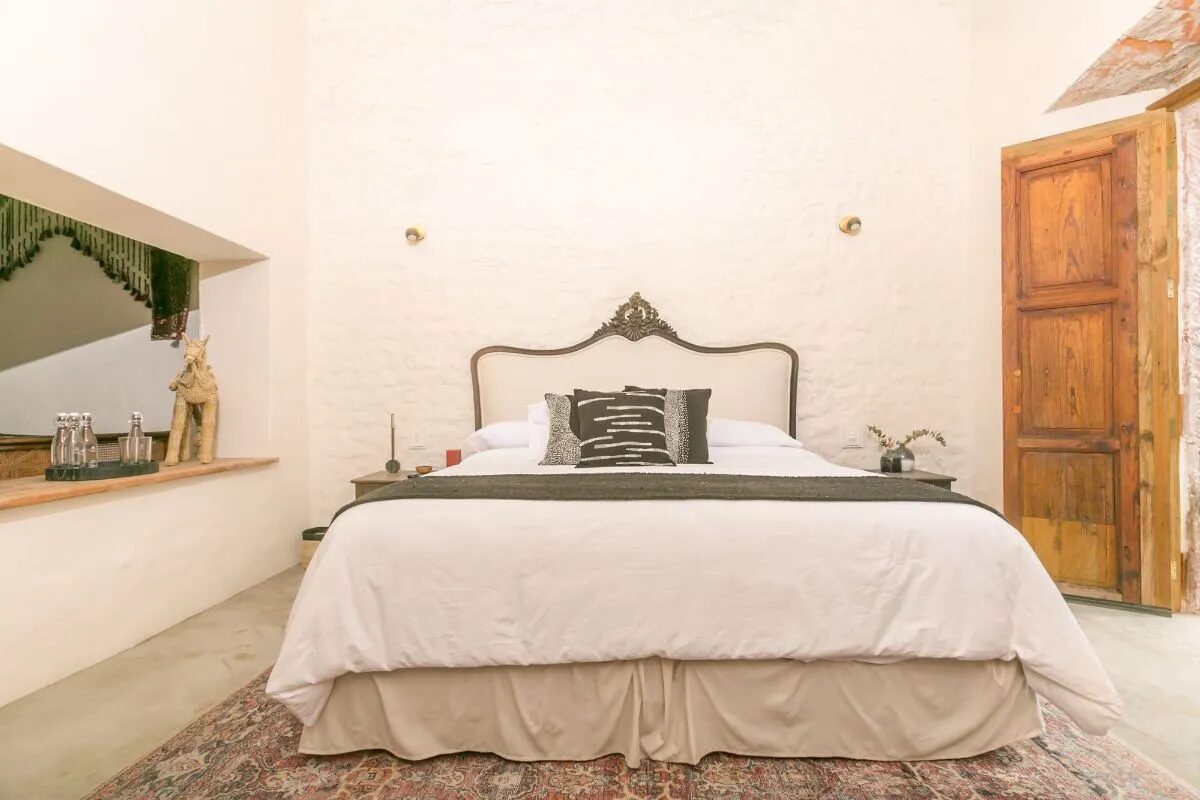 Master suite with a king bed, an upholstered headboard with a carved crest, exposed stucco walls and the original timber door