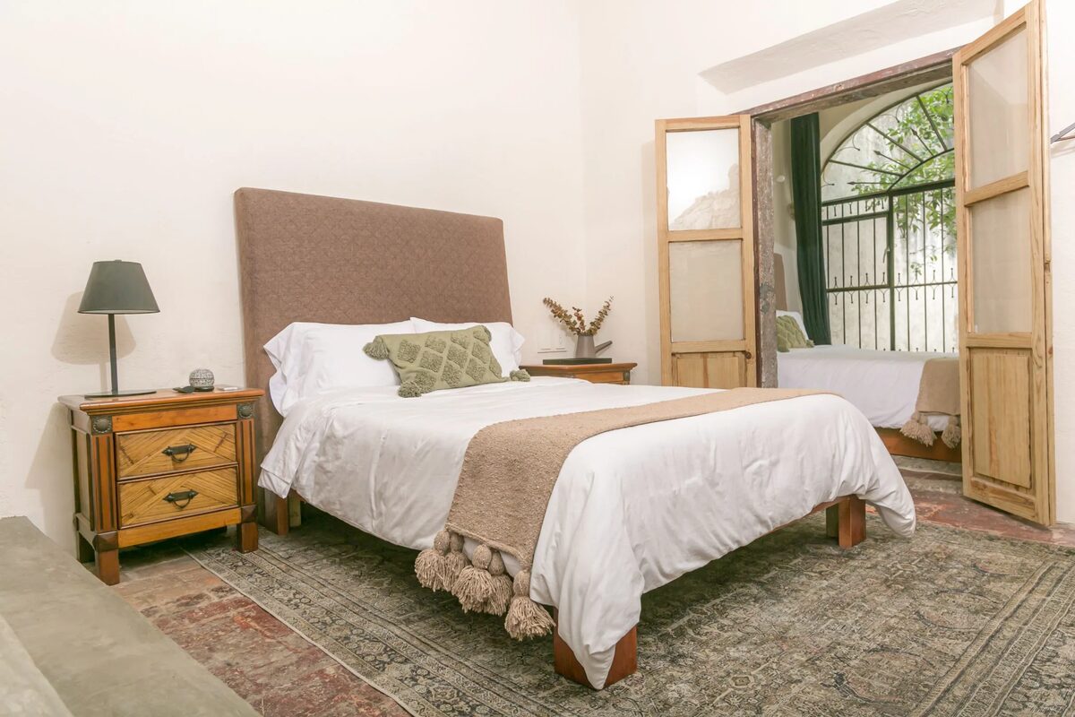 Room with an upholstered headboard and a Persian rug, and through the open door the second queen bed