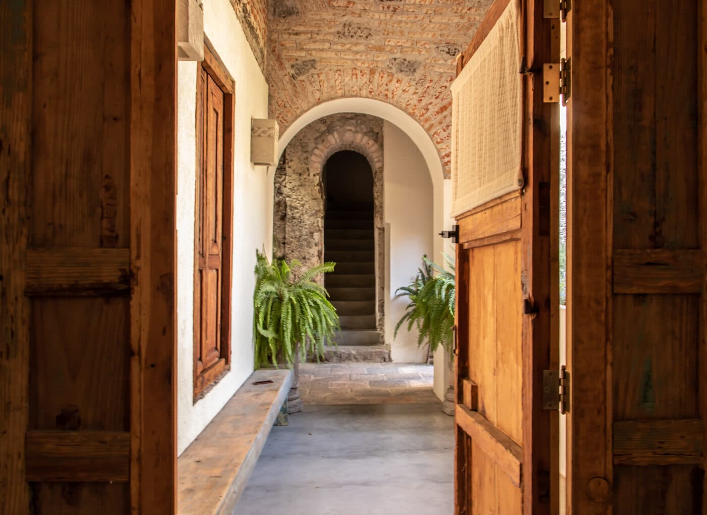 The vaulted brick corridor of the house, with timber doors, a stone bench and the stone staircase beyond, under an arch