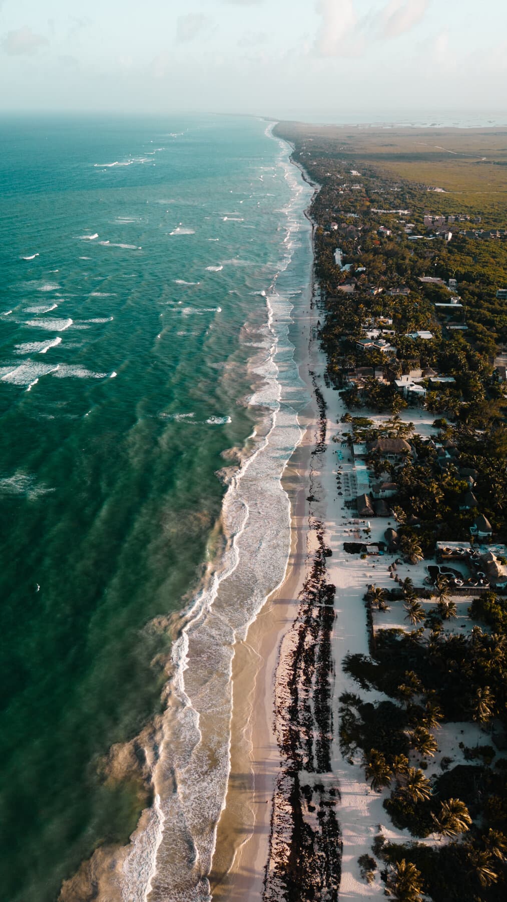 Aerial view of Tulum's Hotel Zone, with the beach, palapa roofs among the palm trees and the access road