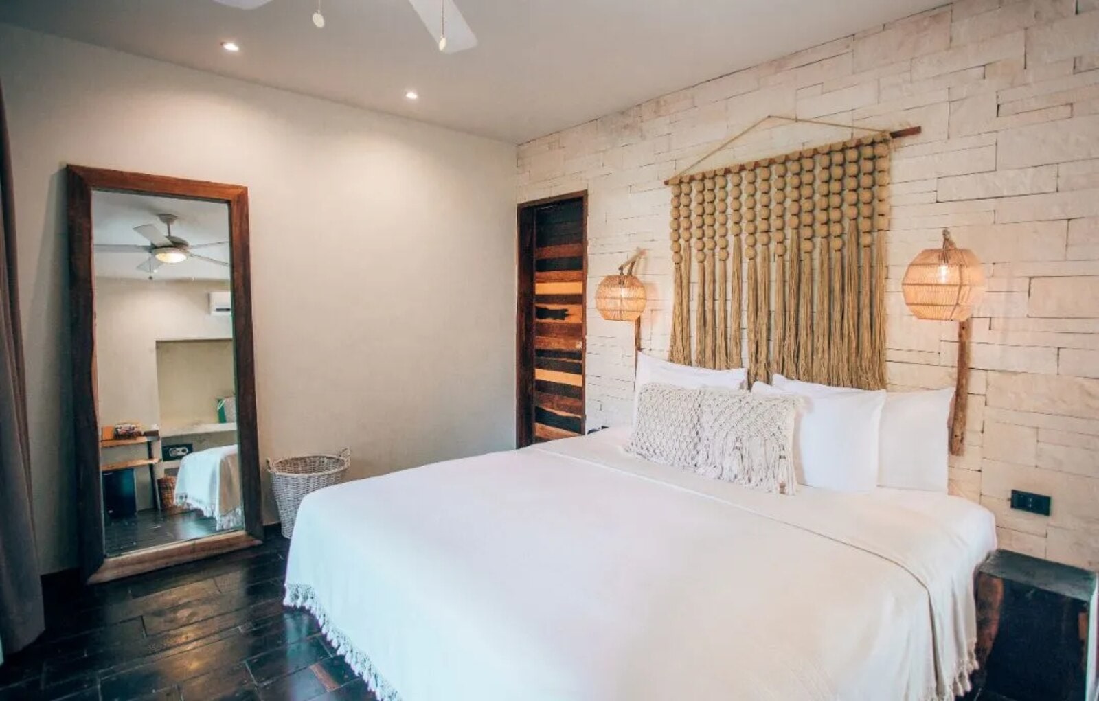 Room with a woven-bead and tassel headboard, and a full-length floor mirror beside the bed
