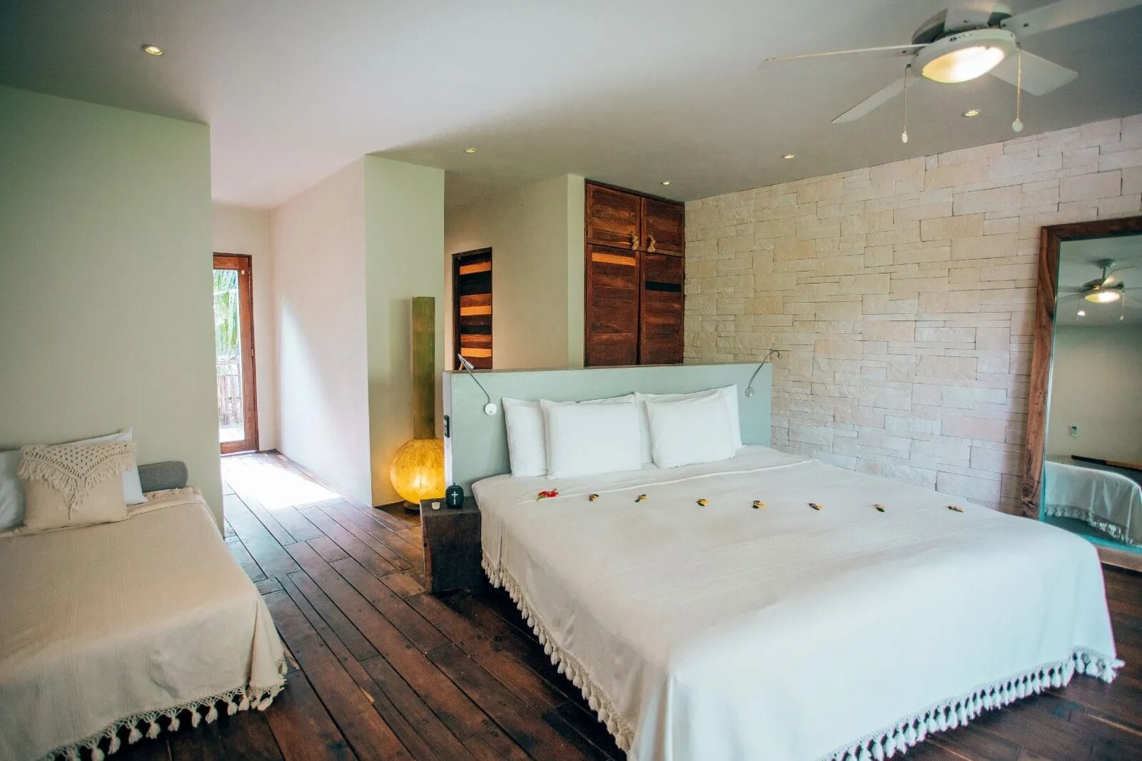 Room with two beds and a hallway leading to an open door with greenery beyond
