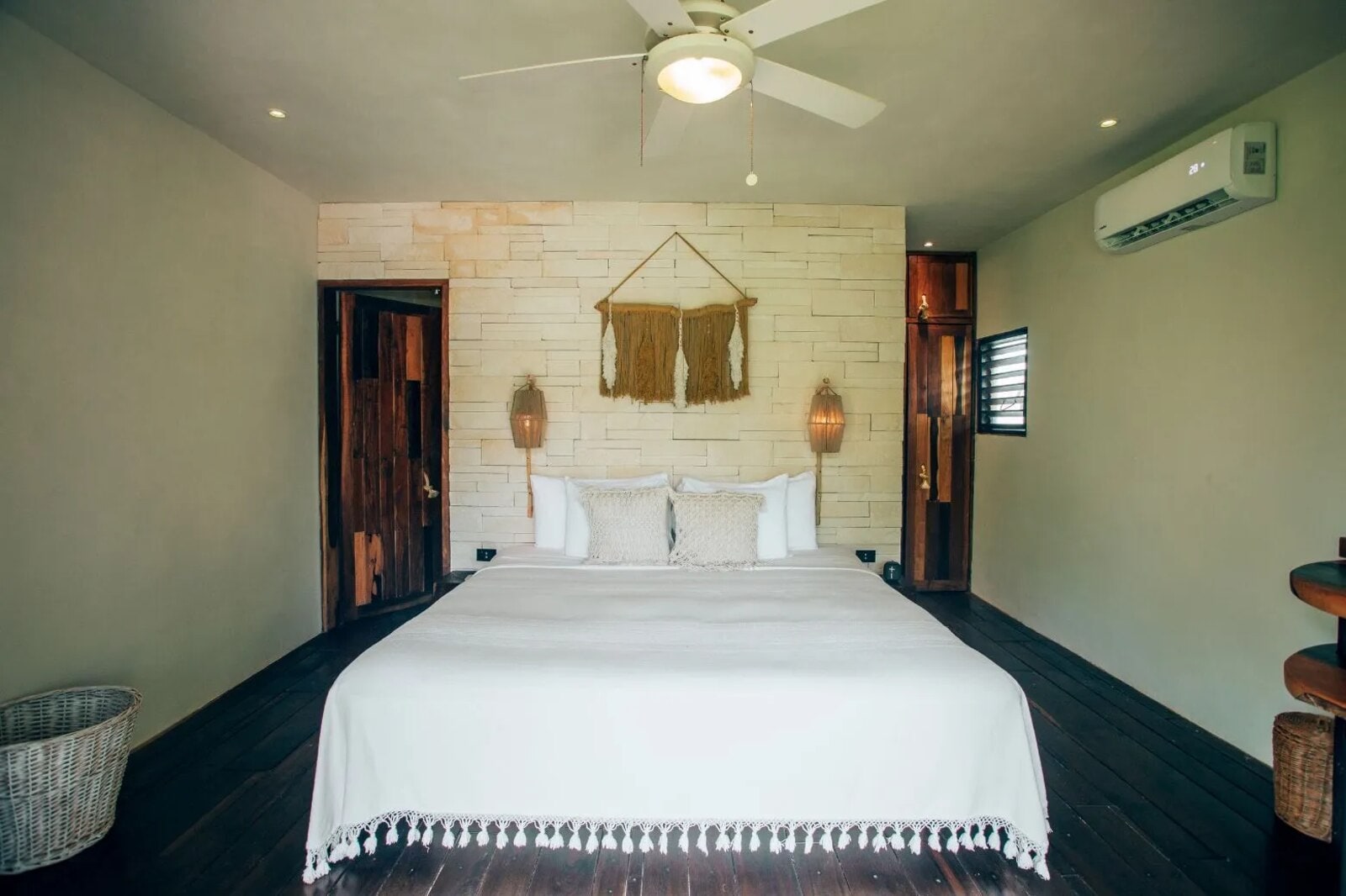 Room with a macramé headboard against a stone wall, a carved timber door and air conditioning