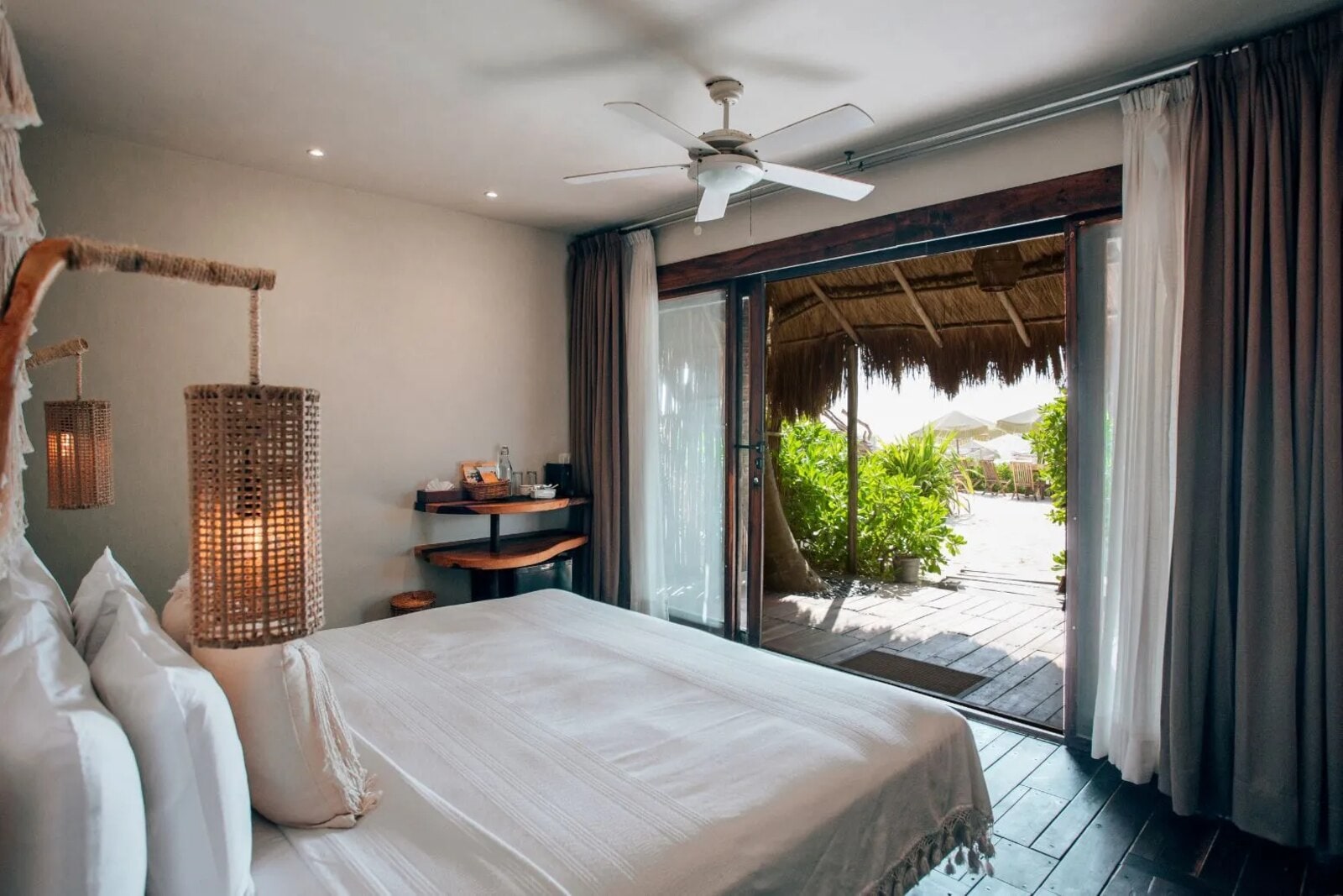 Room with sliding doors open onto an oceanfront palapa, with loungers and umbrellas on the sand