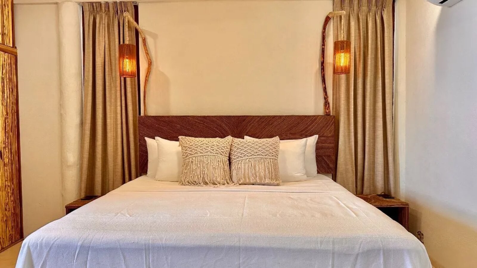 A grained-timber headboard between two hanging wicker lamps, with curtains to either side