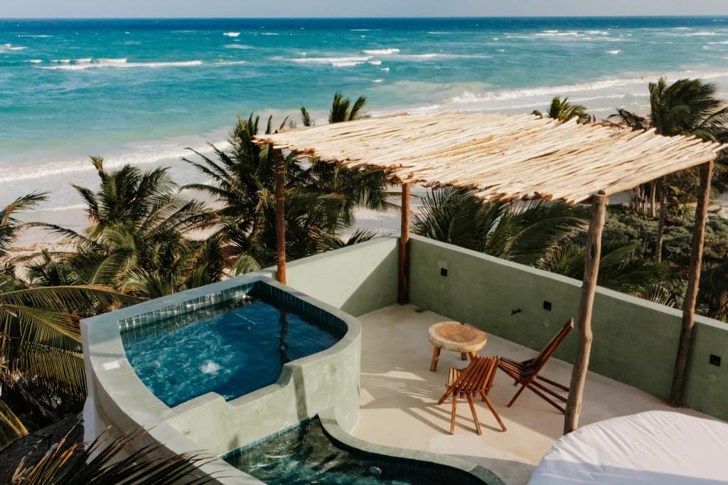 A plunge pool in a rooftop suite, under a palapa, with the Caribbean Sea beyond the palm trees