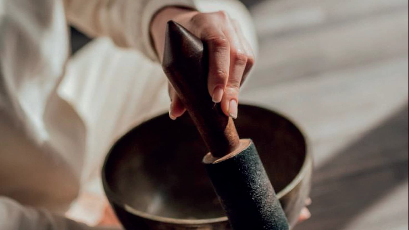 A close-up of a hand holding the mallet of a Tibetan singing bowl, in a sound ritual
